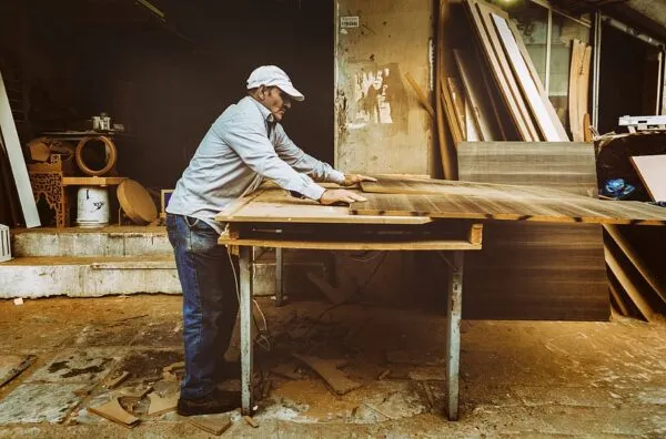 Un carpintero trabajando sobre una mesa de madera en un taller, ajustando tablones de madera en un entorno de oficio tradicional