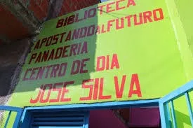 Fachada de un centro comunitario de color verde lima con inscripciones pintadas que indican la presencia de una biblioteca, panadería y el Centro de Día José Silva.