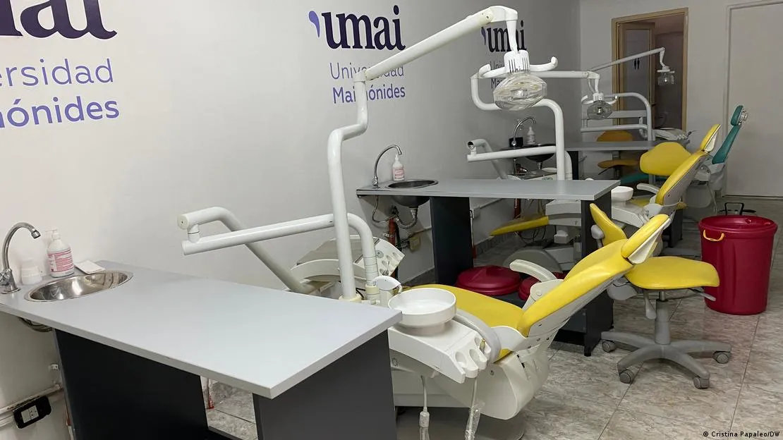 Consultorio odontológico moderno con varios sillones dentales amarillos, equipamiento técnico y logos de la Universidad Maimónides en la pared.
