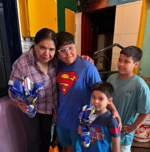 Margarita y tres niños posando sonrientes mientras sostienen huevos de Pascua envueltos en papel brillante azul en un ambiente familiar