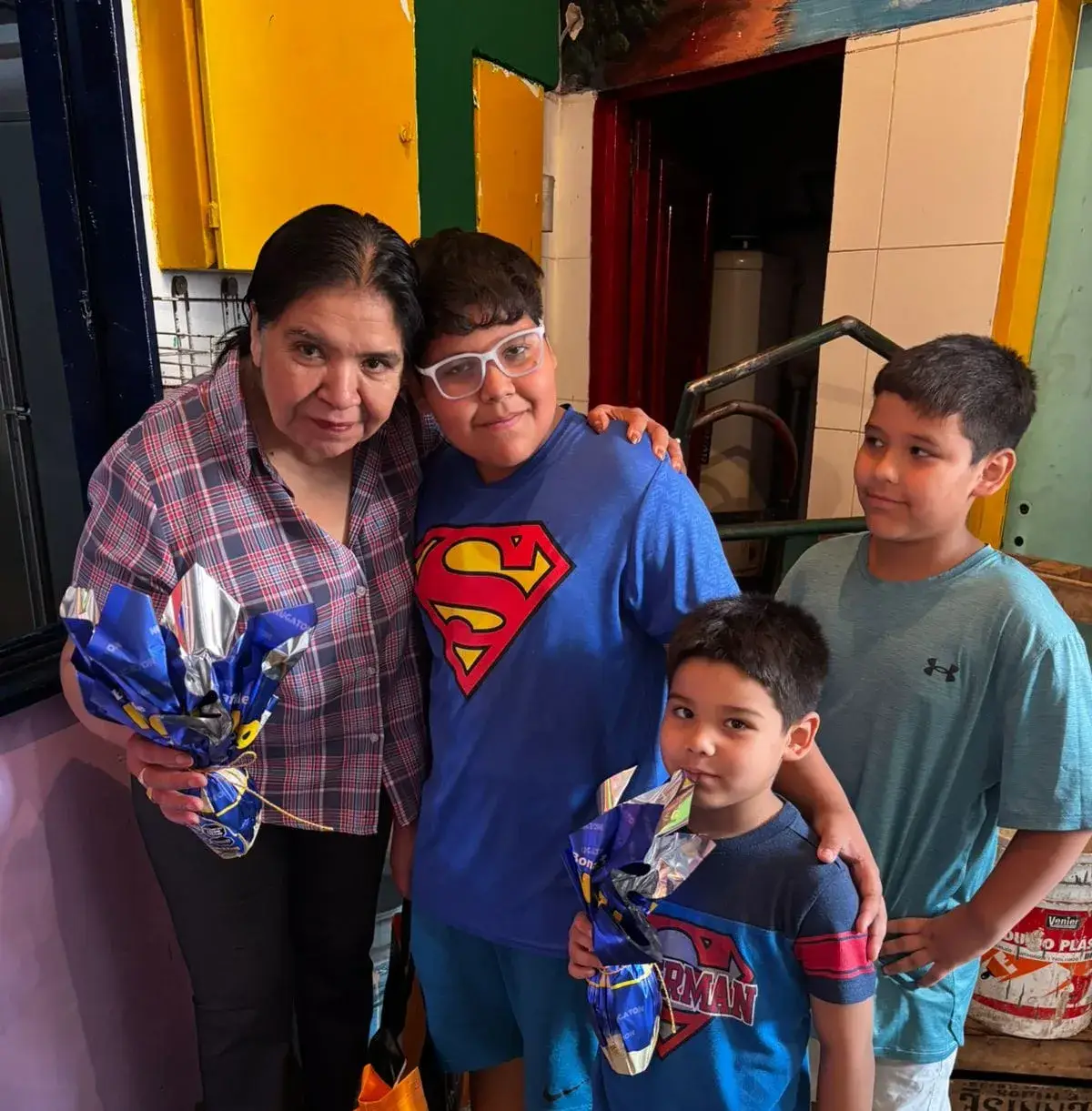 Margarita y tres niños posando sonrientes mientras sostienen huevos de Pascua envueltos en papel brillante azul en un ambiente familiar