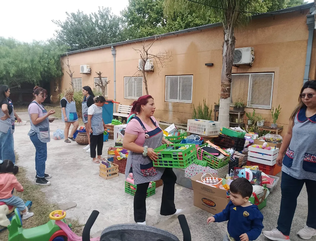 Un grupo de mujeres con pecheras de trabajo organizando cajones con juguetes, libros y materiales recreativos en un patio al aire libre.